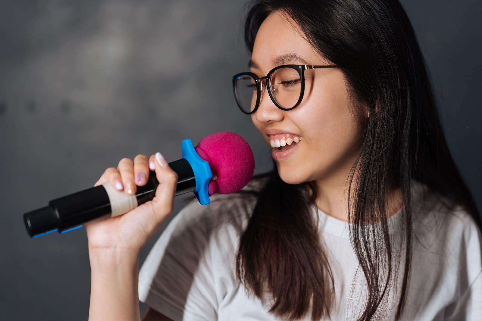 Jovem de óculos cantando karaokê ao microfone, sorrindo